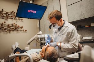 Dr. Baltz treating patient while they relax watching netflix